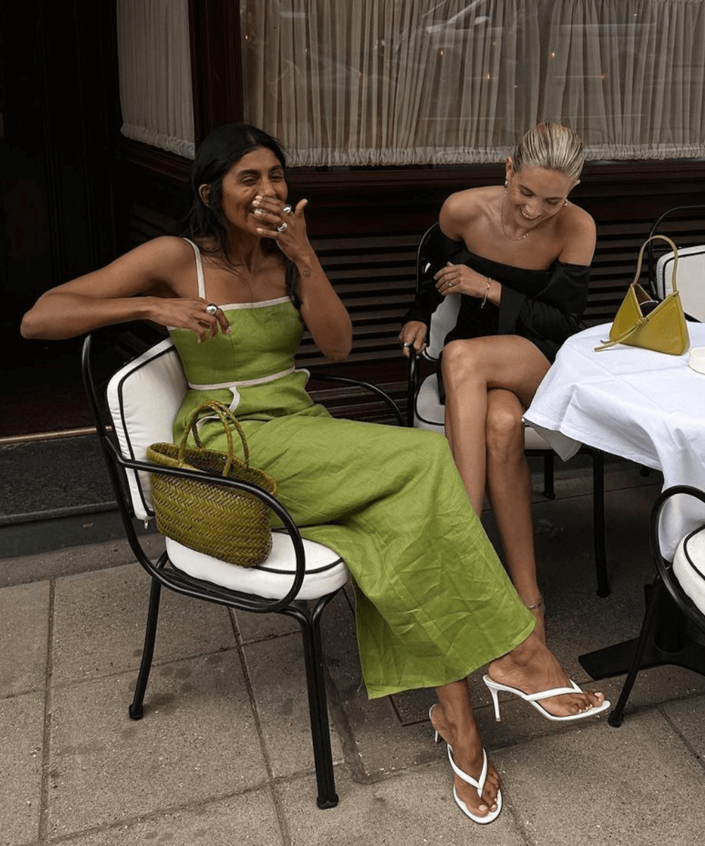 @monikh - vestido longo verde e tamanco de salto fino - sandálias da moda - verão - mulher sentada em uma mesa rindo ao lado de uma amiga loira - https://stealthelook.com.br