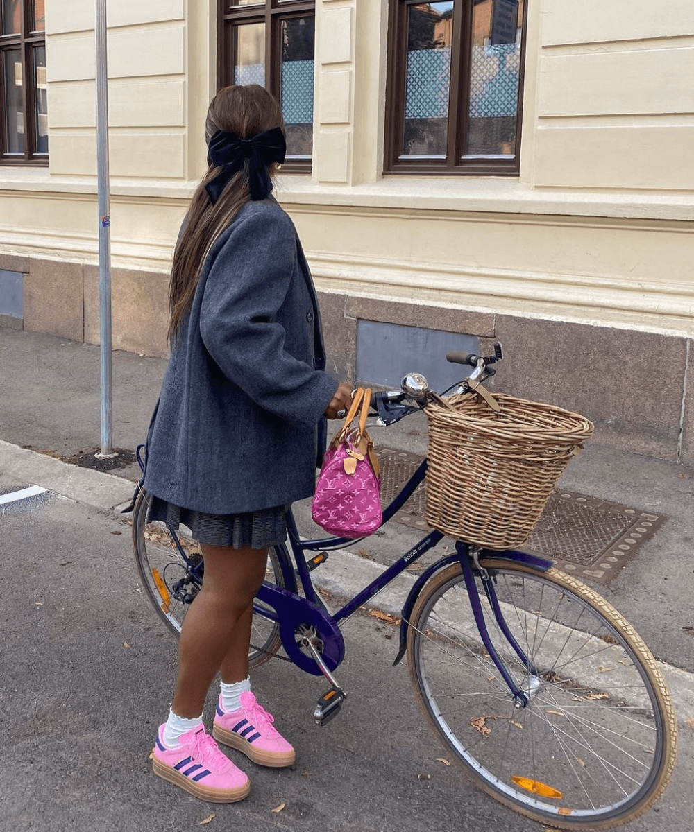 Nnenna Echem - minissaia plissada, t-shirt preta, tênis rosa e blazer - tênis colorido - primavera - mulher negra de costas segurando uma bike na rua - https://stealthelook.com.br