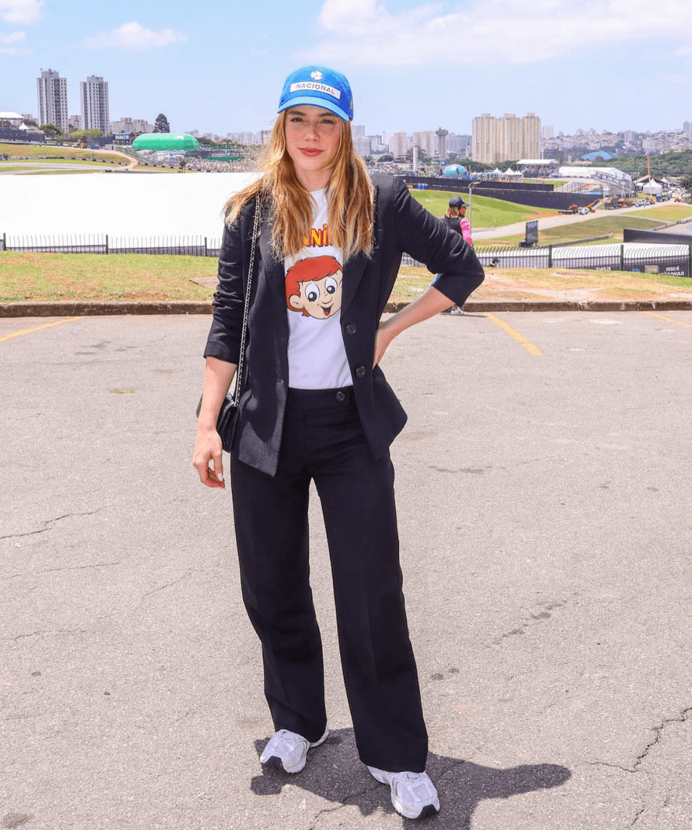 Alice Wegmann - calça preta, blusa do senninha, boné azul e blazer preto - looks do GP da Fórmula 1 - primavera - mulher em pé usando boné - https://stealthelook.com.br