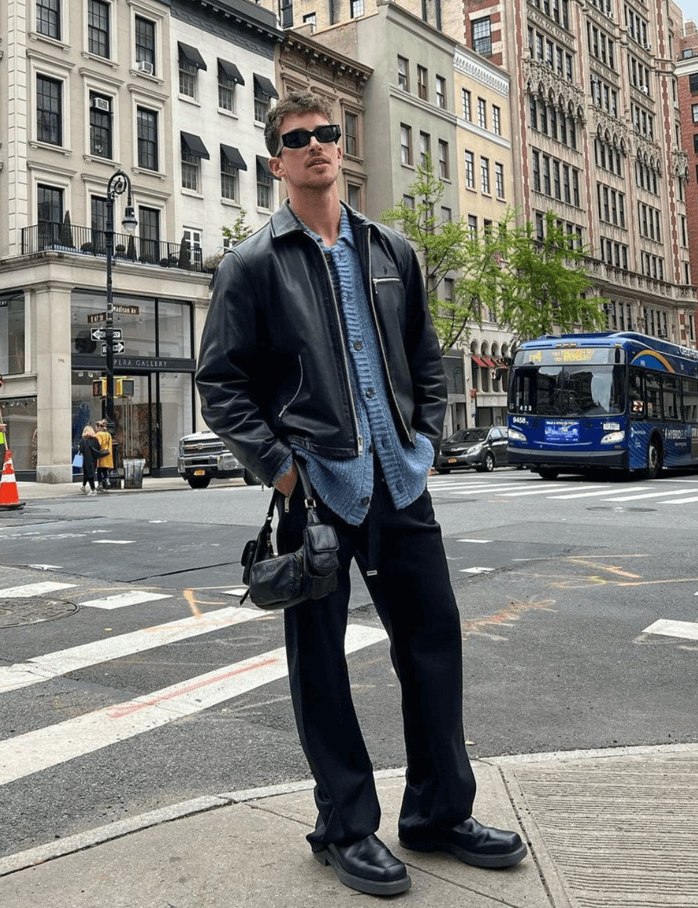 Manu Rios - calça, camisa, jaqueta jeans, bolsa de mão preta e óculos - homens usando bolsas - inverno - homem parado em pé na rua usando óculos de sol - https://stealthelook.com.br