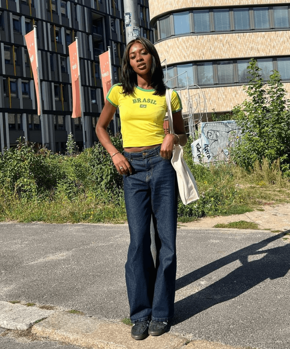 @georgia_3.0 - calça jeans flare, blusa baby tee do brasil e tênis - look para o show do RBD - outono - mulher negra em pé na rua - https://stealthelook.com.br