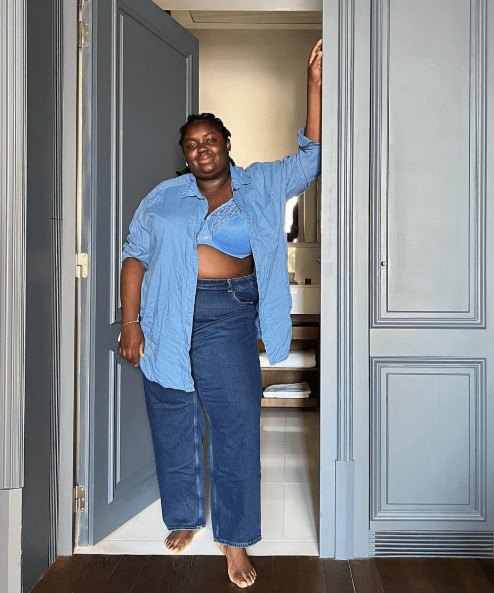 Abisola Omole - calça jeans e camisa azul social - Black Friday - primavera - mulher negra em pé em uma sala encostada em uma porta azul - https://stealthelook.com.br