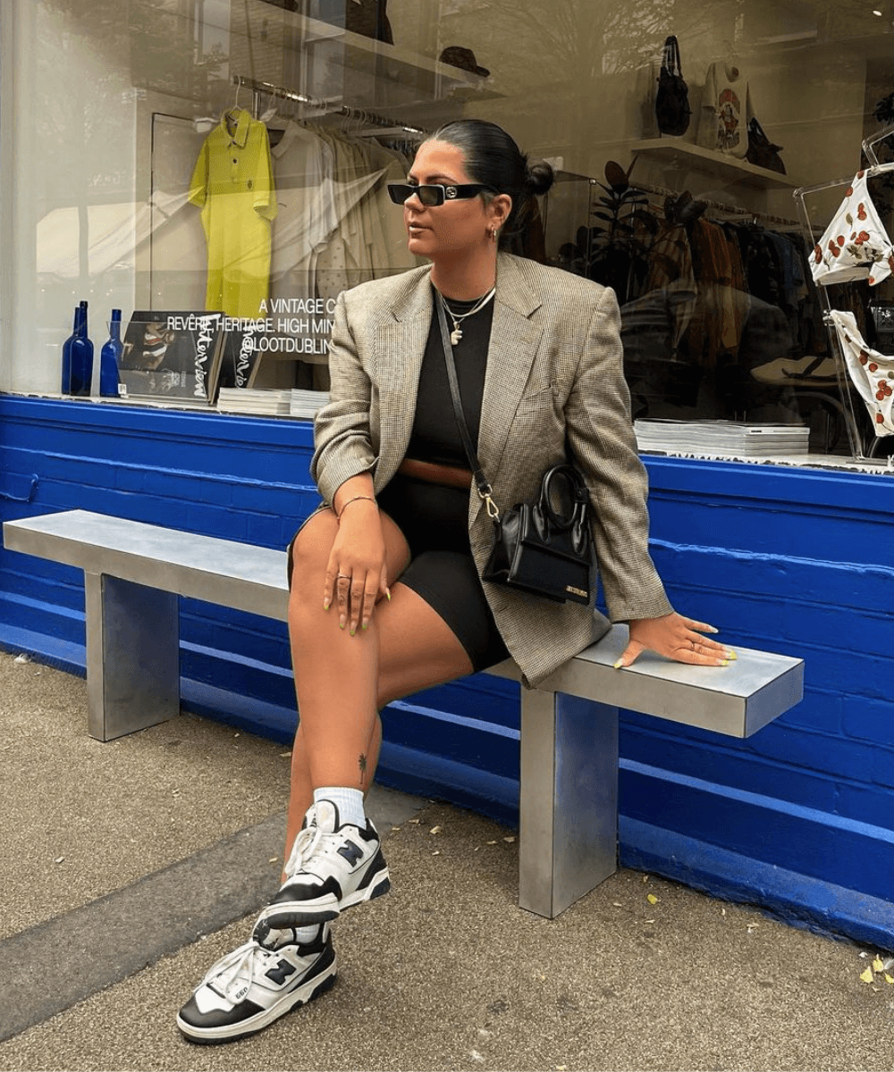 Freya Broni - set de academia preto, blazer oversized, óculos e tênis new balance - peças-chave estilosas - outono - mulher sentada em um banco na rua - https://stealthelook.com.br