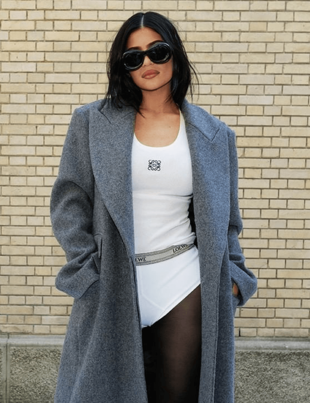 Kylie Jenner - micro shorts branco, regata, scarpin, sobretudo oversized cinza e óculos de sol - Principais tendências 2023 - outono - mulher morena em pé na rua usando óculos de sol - https://stealthelook.com.br