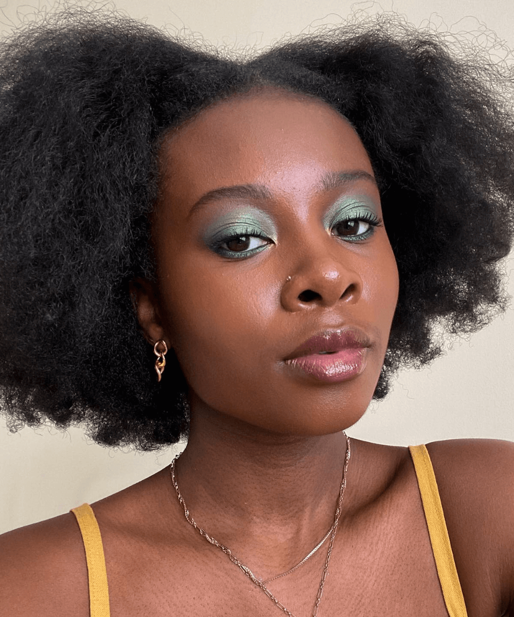 Damola Akintunde - blusa alcinha amarela - maquiagem para a the eras tour - verão - foto de close do rosto de uma mulher negra usando maquiagem verde - https://stealthelook.com.br
