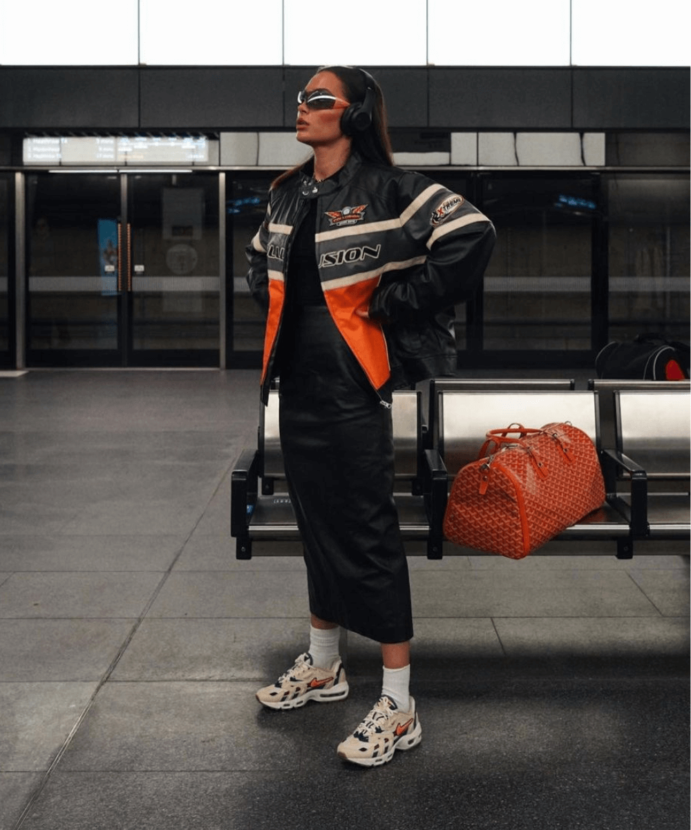Alicia Roddy - saia midi de couro, tênis nike alaranjado e casaco esportivo laranja - sportswear - outono - mulher em pé em um metrô usando óculos de sol - https://stealthelook.com.br