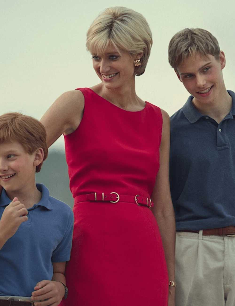 Elizabeth Debicki - vestido midi vermelho - Looks da Princesa Diana - verão - atriz de pé em barco ao lado de dois atores menores  - https://stealthelook.com.br