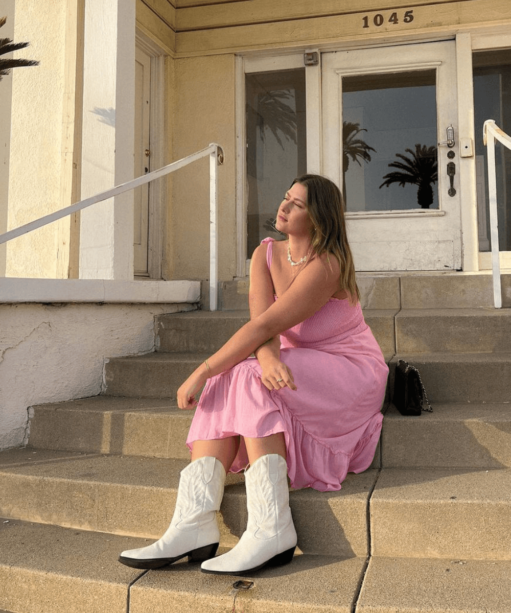 Raeann Langas - vestido midi rosa e botas western - vestido midi soltinho - verão - mulher loira sentada em uma escada na rua - https://stealthelook.com.br