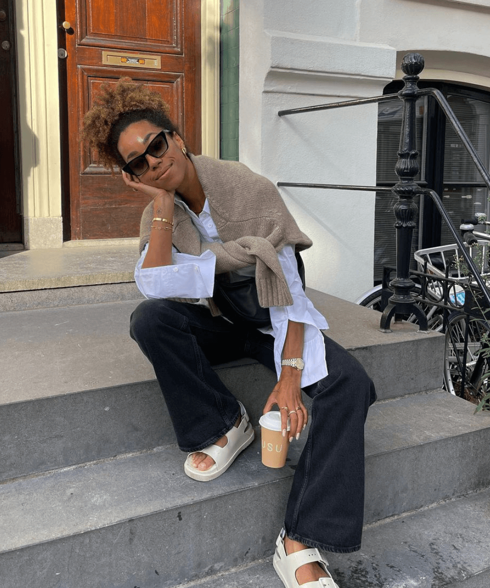 Amaka Hamelijnck - calça flare, papete, camisa branca e óculos escuros - tendências polêmicas - outono - mulher negra sentada na rua usando óculos de sol com as pernas dobradas - https://stealthelook.com.br