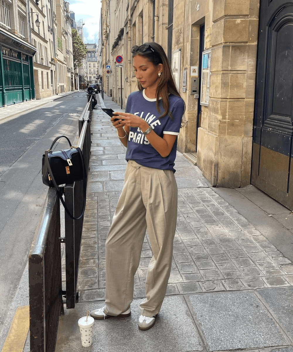 Felicia Akerstrom - calça de alfaiataria bege, t-shirt azul e tênis - blusas femininas da moda - verão - mulher em pé na rua mexendo no celular - https://stealthelook.com.br