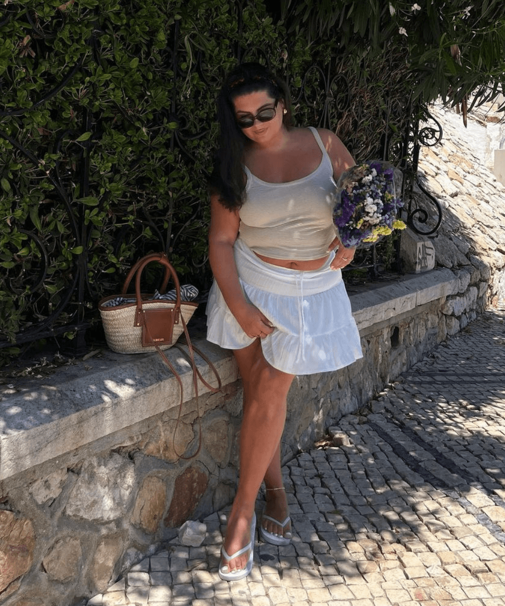 Freya Broni - minissaia rodada, regata branca e chinelo branco - blusas femininas da moda - verão - mulher em pé na rua usando óculos de sol - https://stealthelook.com.br