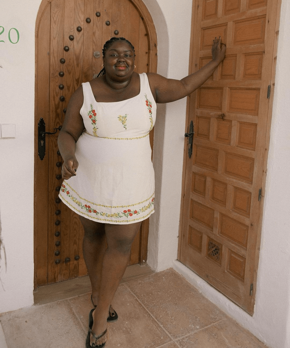 Abisola Omole - vestido curto estampado branco e chinelo preto - looks com chinelo - verão - mulher negra em pé na rua sorrindo  - https://stealthelook.com.br