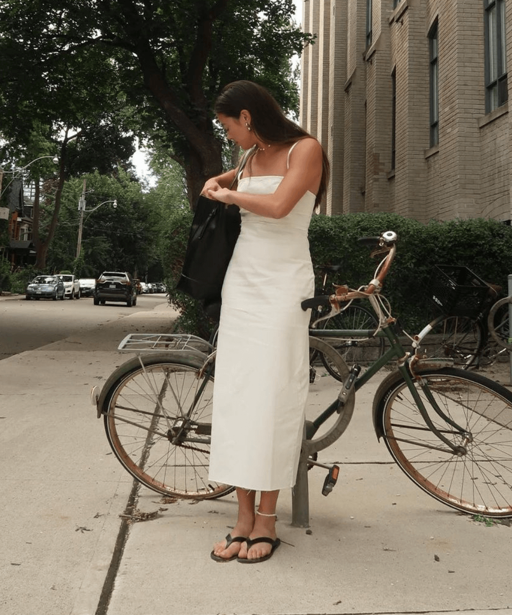 Sasha Mei - vestido midi branco e chinelo preto - looks com chinelo - verão - mulher asiática em pé na rua na frente de uma bicicleta - https://stealthelook.com.br