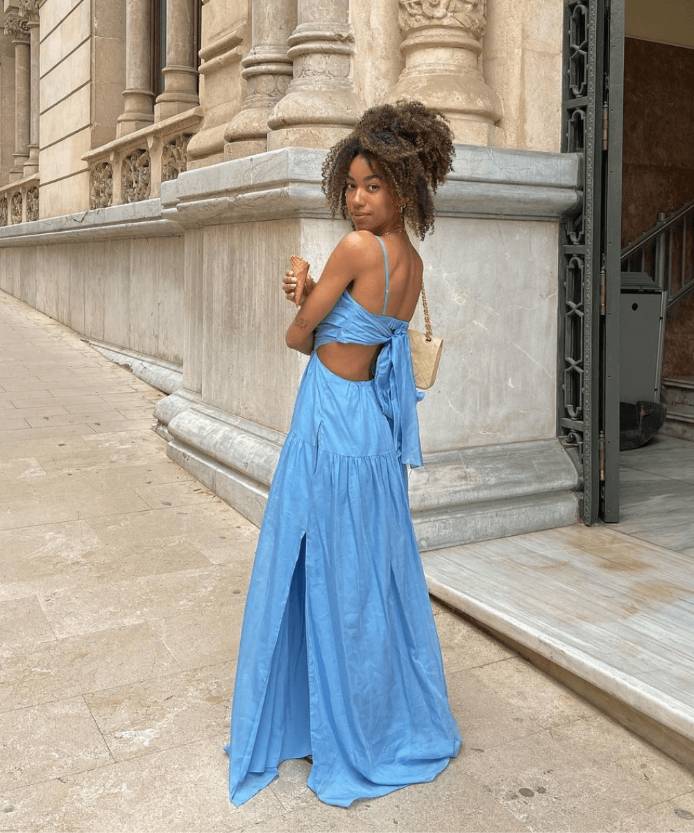 Amaka Hamelijnck - vestido longo azul de costas de fora - look da virada - verão - mulher negra em pé na rua de costas - https://stealthelook.com.br
