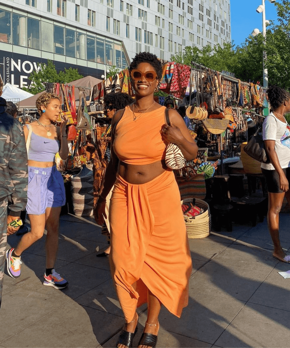 Yolande Macon - conjunto laranja de saia midi e cropped - look da virada - verão - mulher negra em pé na rua usando óculos de sol - https://stealthelook.com.br
