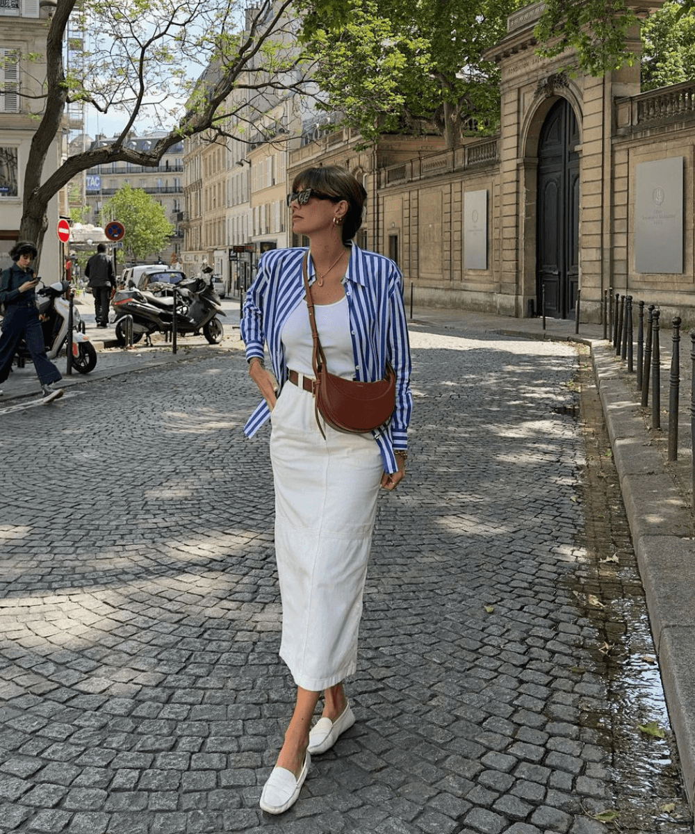 Julie Sergent Ferreri - saia midi branca, regata, camisa azul listrada e mocassim branco - looks com saia midi - verão - mulher de óculos em pé na rua - https://stealthelook.com.br