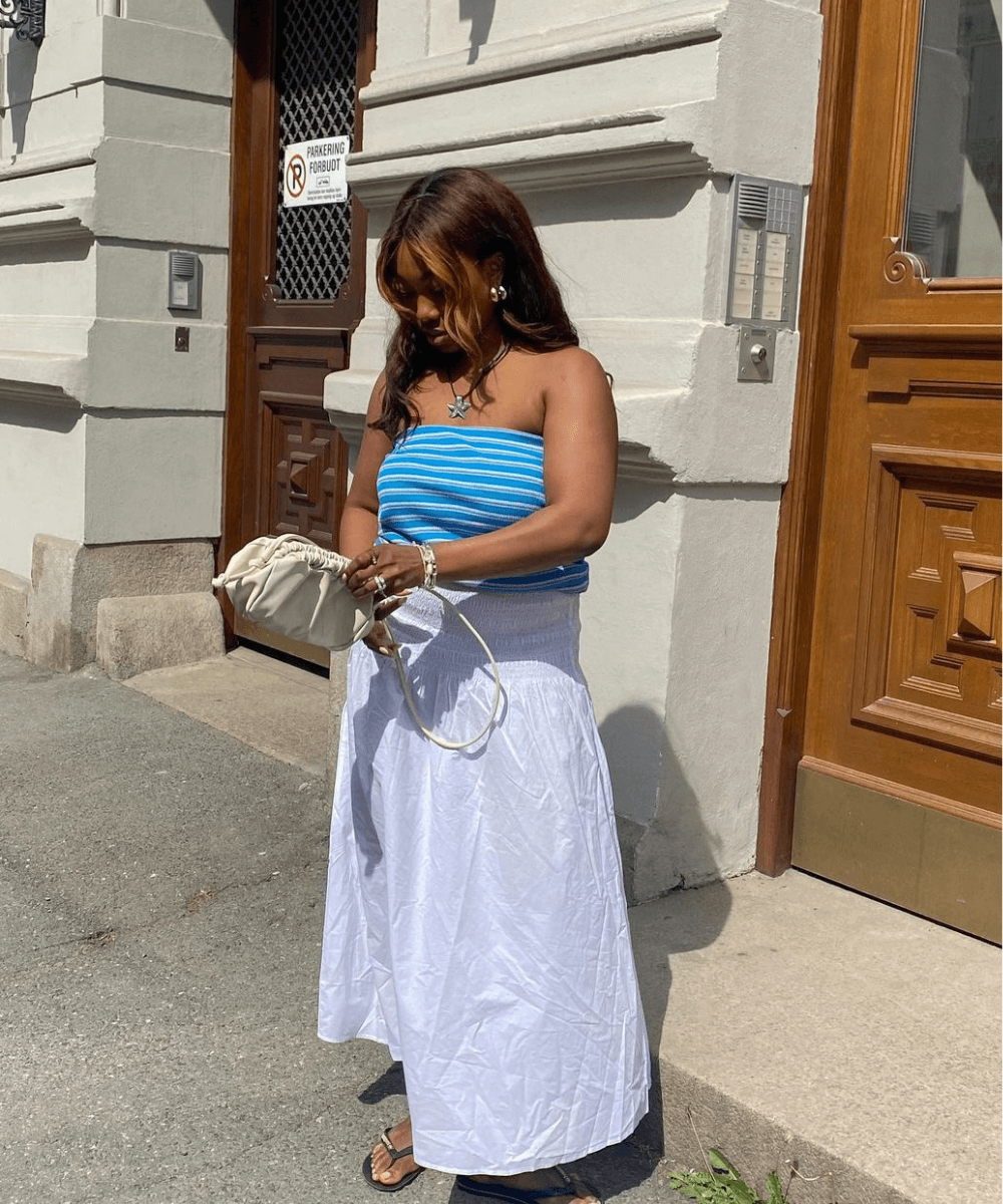 Nnenna Echem - saia midi branca, top azul listrado e chinelo havainas - looks com saia midi - verão - mulher negra em pé na rua - https://stealthelook.com.br