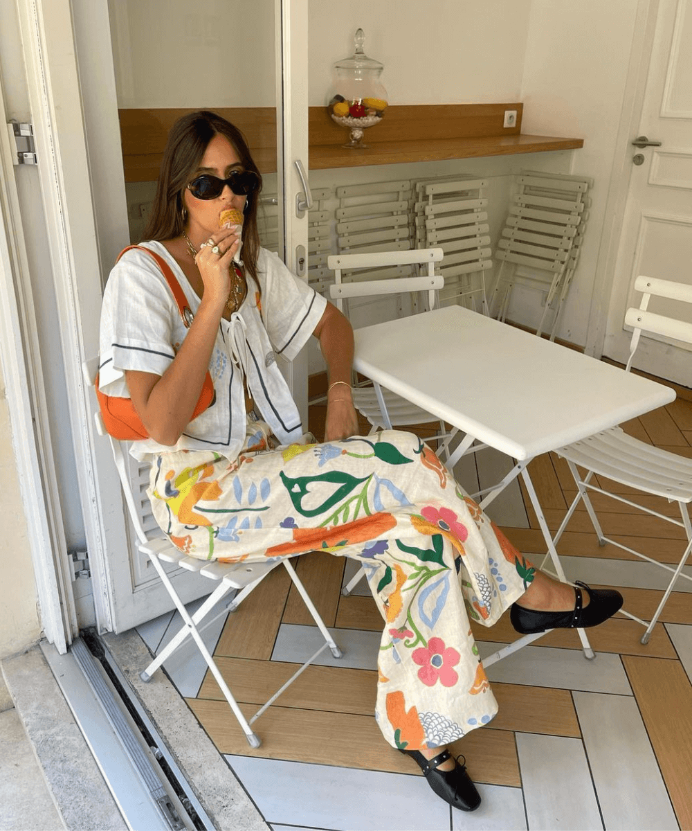 @florettenacer - calça estampada colorida, blusa de amarração e sapatilha preta bailarina - looks fáceis e fresquinhos - verão - mulher sentada em uma cadeira na rua tomando sorvete de casquinha - https://stealthelook.com.br