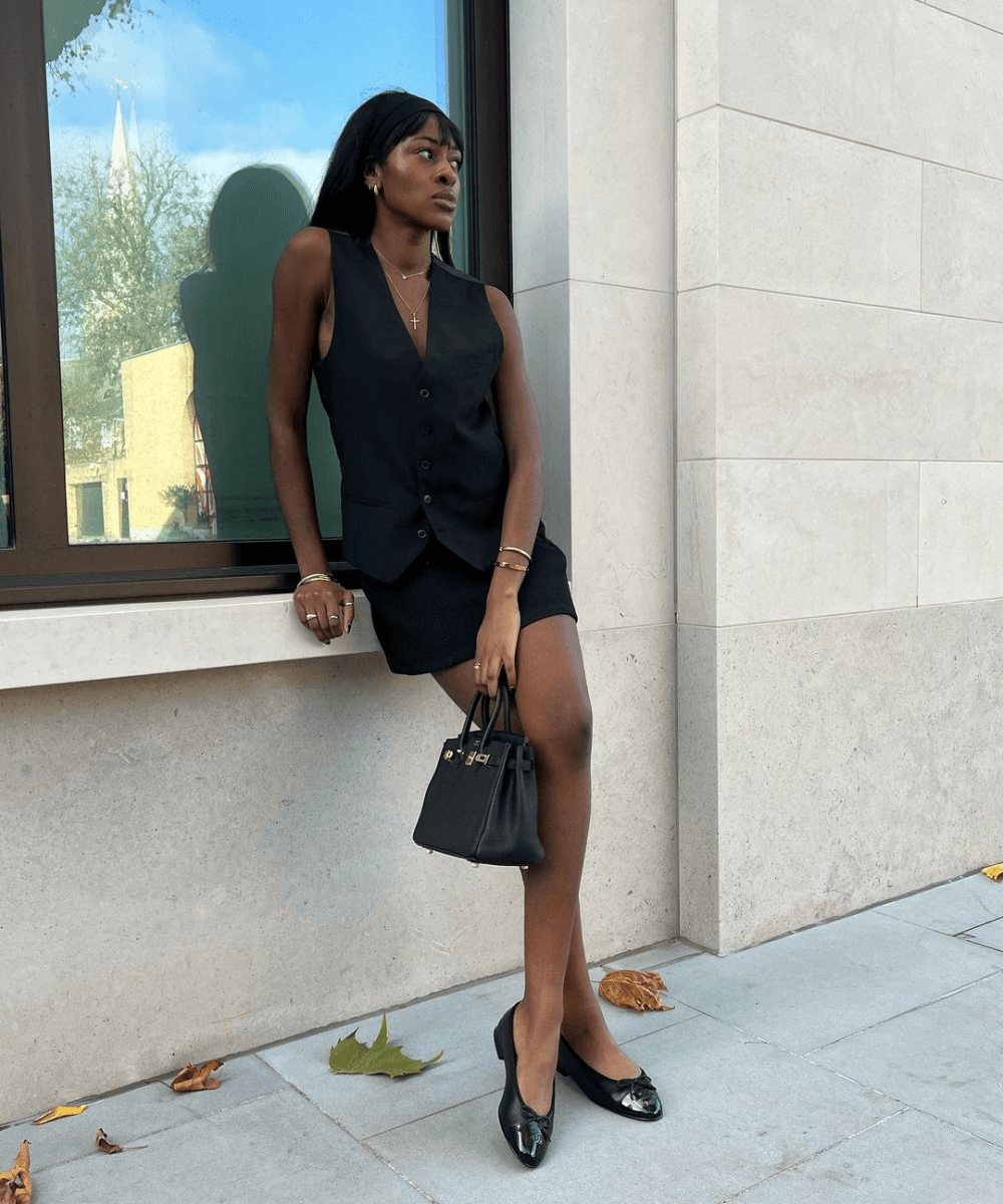 @georgia_3.0 - minissaia preta, colete de alfaiataria preto e sapatilha preta - looks fáceis e fresquinhos - verão - mulher negra em pé na rua - https://stealthelook.com.br