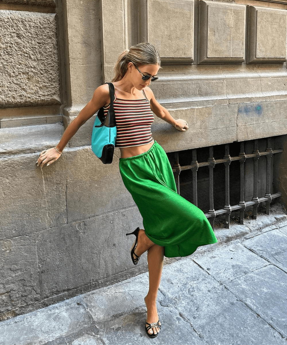 Emili Sindlev - saia midi verde, top cropped listrado e tamanco preto - sapato elegante - verão - mulher loire de óculos em pé na rua encostada em um muro com uma das pernas dobradas - https://stealthelook.com.br