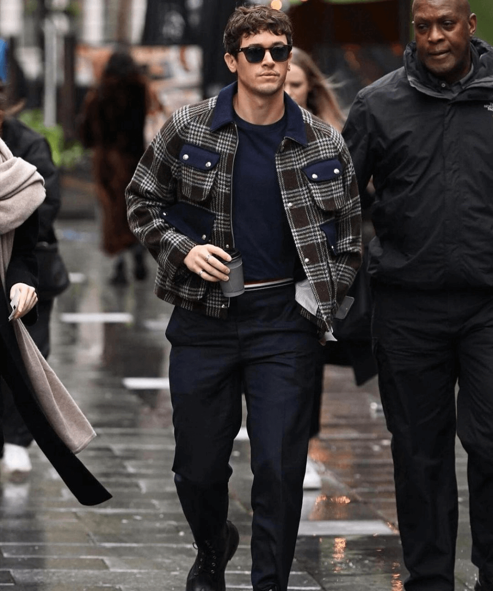 Tom Blyth - calça preta, suéter azul marinho, jaqueta xadrez - Tom Blyth - inverno - homem de óculos andando na rua - https://stealthelook.com.br