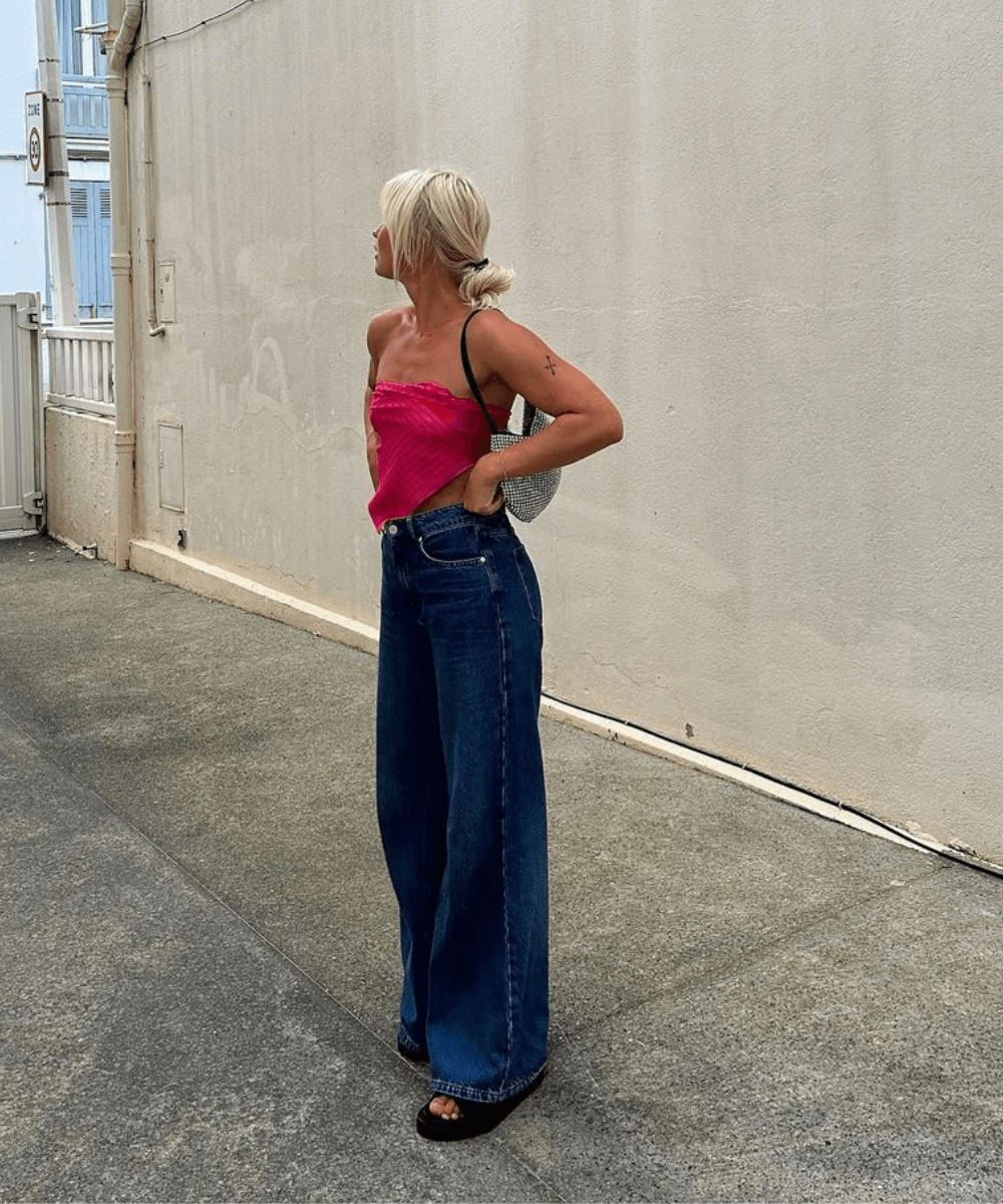 Amanda Djerf - calça jeans pantalona, top de amarrar rosa e chinelos - looks fresquinhos - verão - mulher loira em pé na rua - https://stealthelook.com.br