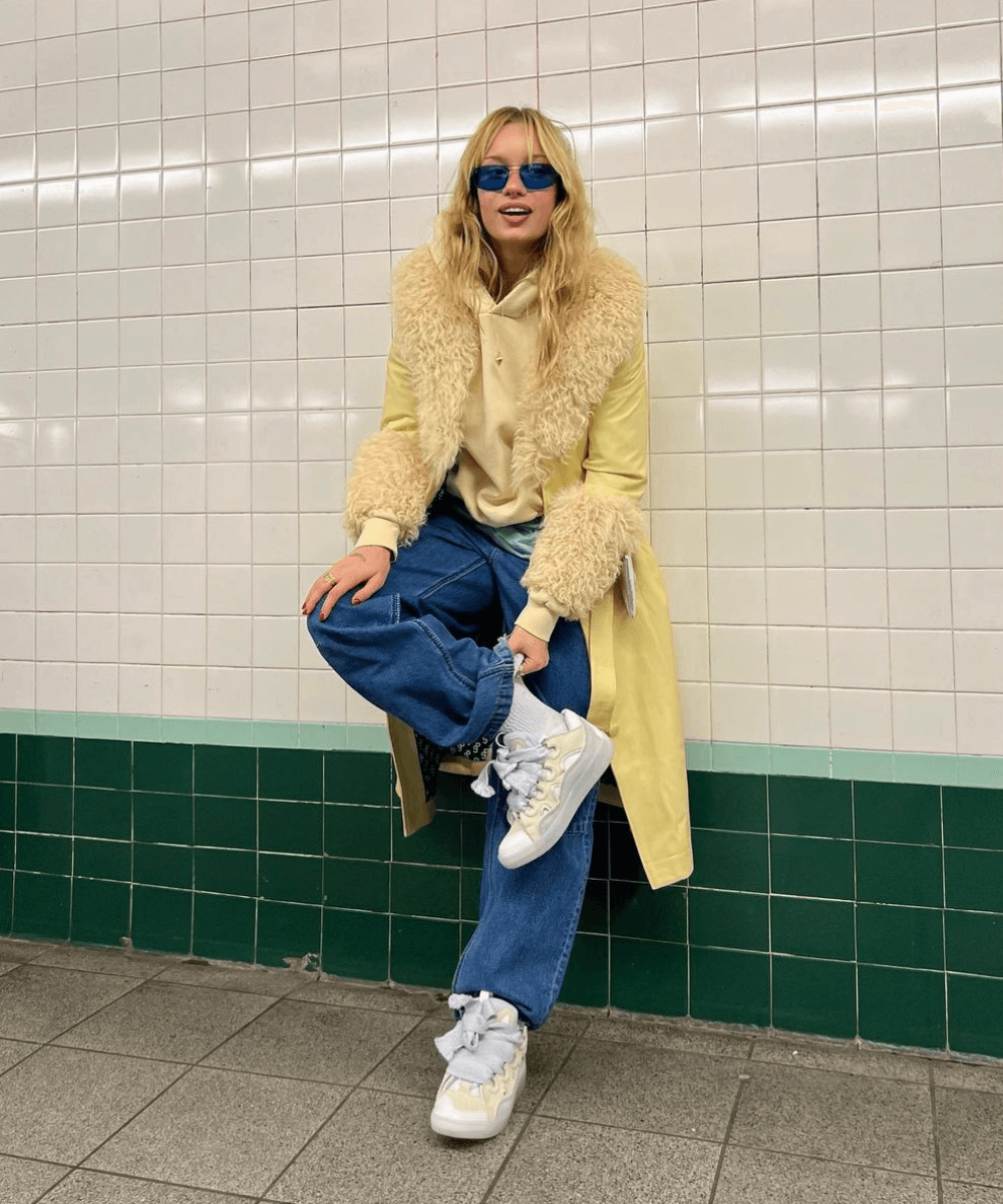 @linmick - calça jeans, tênis, casaco penny lane e moletom amarelo claro - tendência do inverno 2024 - inverno - mulher loira andando na rua usando óculos de sol - https://stealthelook.com.br