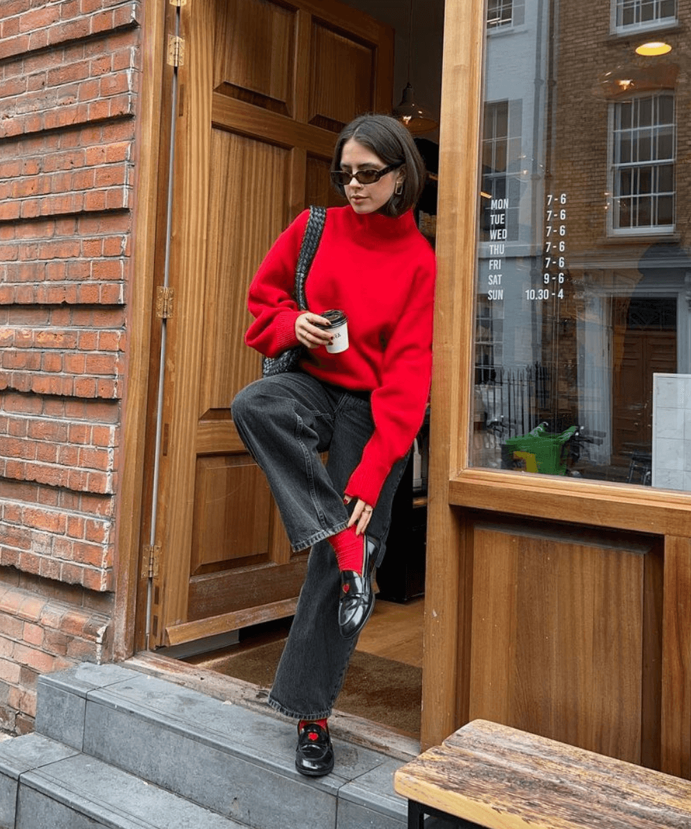 Tia Dewitt - tricot vermelho, calça jeans preta, meias vermelhas e mocassins - inverno 2024 - inverno - mulher de cabelos castanhos usando óculos de sol em pé na rua - https://stealthelook.com.br