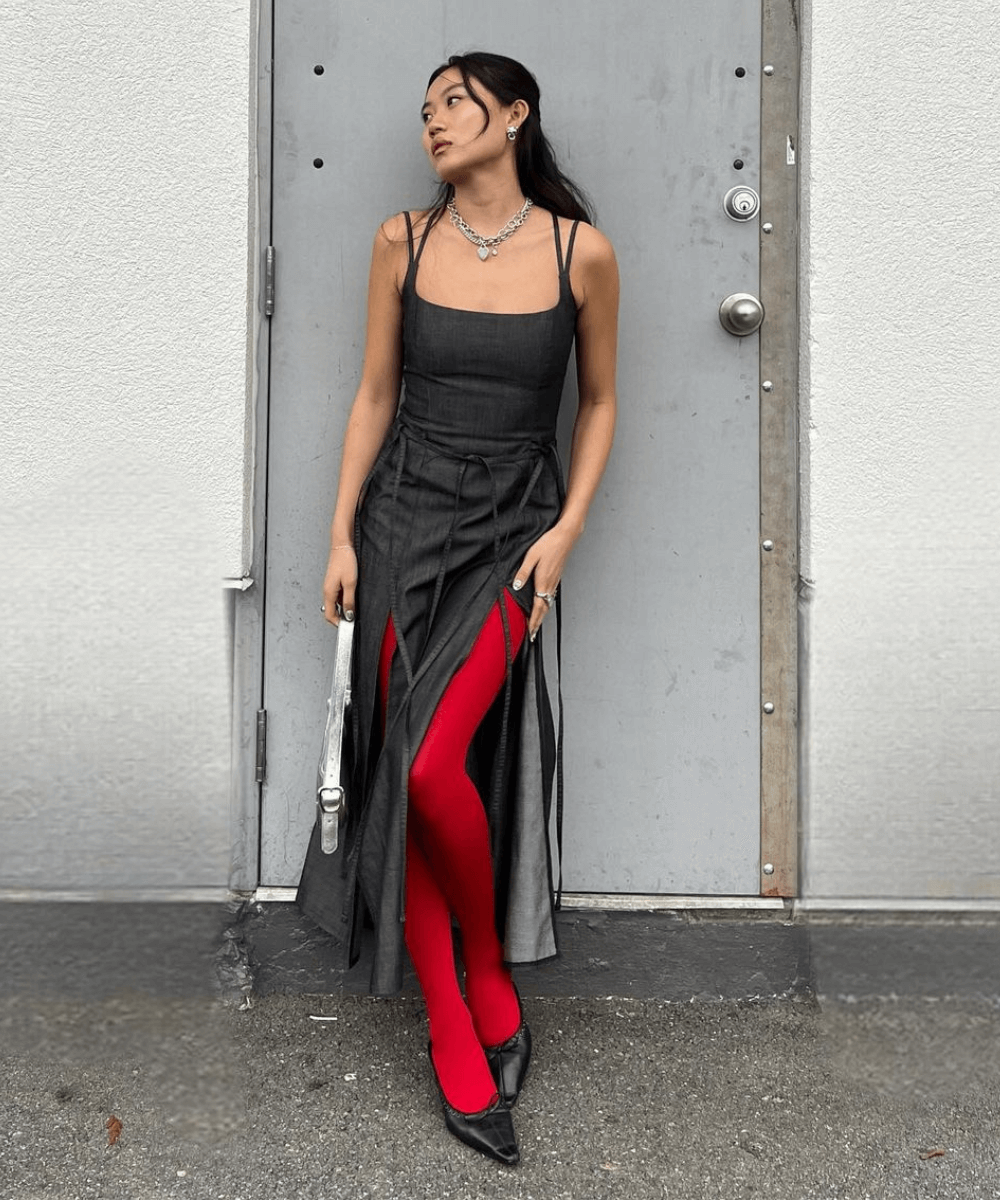 @vivian.yrl - vestido preto midi, meia-calça vermelha e sapatilhas pretas - inverno 2024 - outono - mulher asiática em pé encostada em um parede cinza na rua - https://stealthelook.com.br