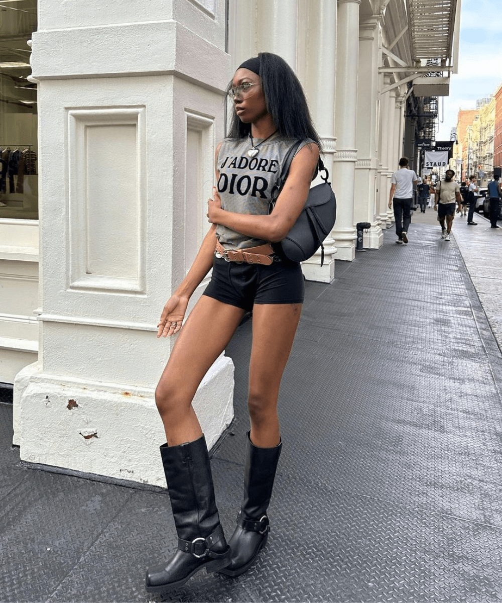 Chanel Mckinsie - mini shorts preto, bota de cano longo, regata justa, cintos e óculos - looks de festival - verão - mulher negra em pé na rua usando óculos de sol - https://stealthelook.com.br