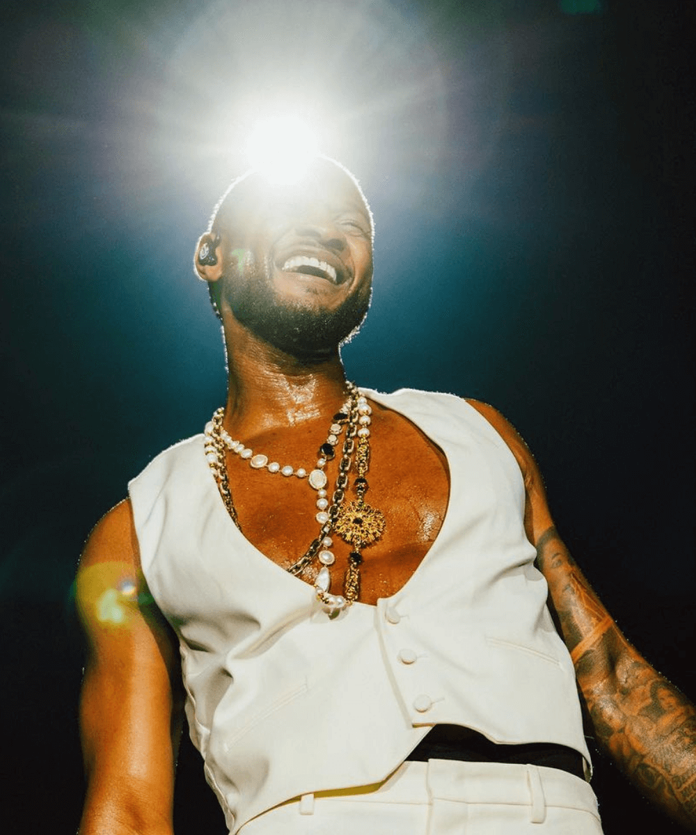 Usher - colete branco e calça branca de alfaiataria - Super Bowl 2024 - inverno - homem negro usando vários colares sorrindo em um palsco - https://stealthelook.com.br