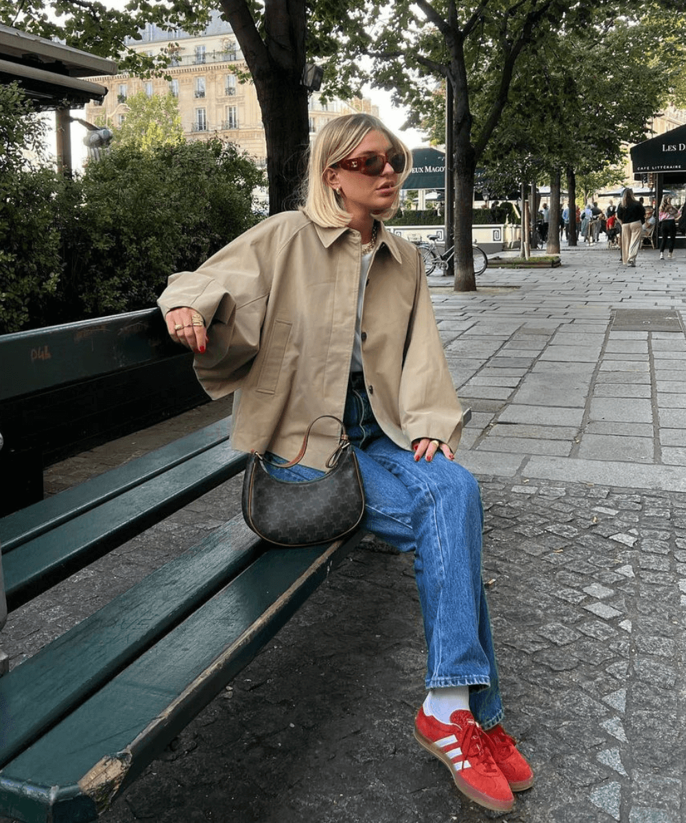 Audrey Afonso - calça jeans, tênis vermelho adidas, camisa branca e trench coat - sapato vermelho - inverno - mulher loira de óculos sentada em um banco na rua - https://stealthelook.com.br