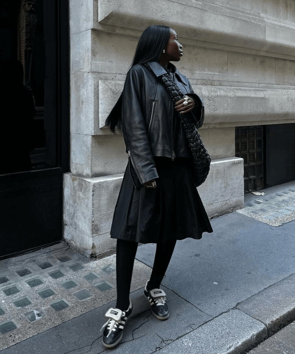 Danielle Oreoluwa Jinadu - saia midi preta, meia-calça preta, tênis adidas preto e jaqueta de couro preta - jaqueta de couro - inverno - mulher negra em pé na rua usando óculos de sol - https://stealthelook.com.br