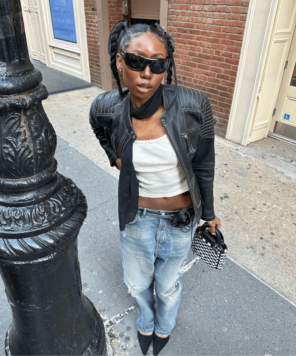 Chanel Mckinsie - calça jeans, blusa branca, jaqueta de couro, bota e bolsa - jaqueta de couro - inverno - mulher negra em pé na rua usando óculos de sol - https://stealthelook.com.br