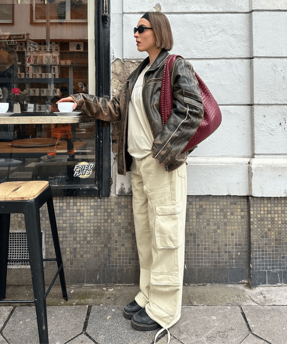 @lara_bsmnn - calça bege, moletom bege, jaqueta de couro marrom e mocassim - jaqueta de couro - inverno - mulher em pé na rua usando óculos de sol - https://stealthelook.com.br