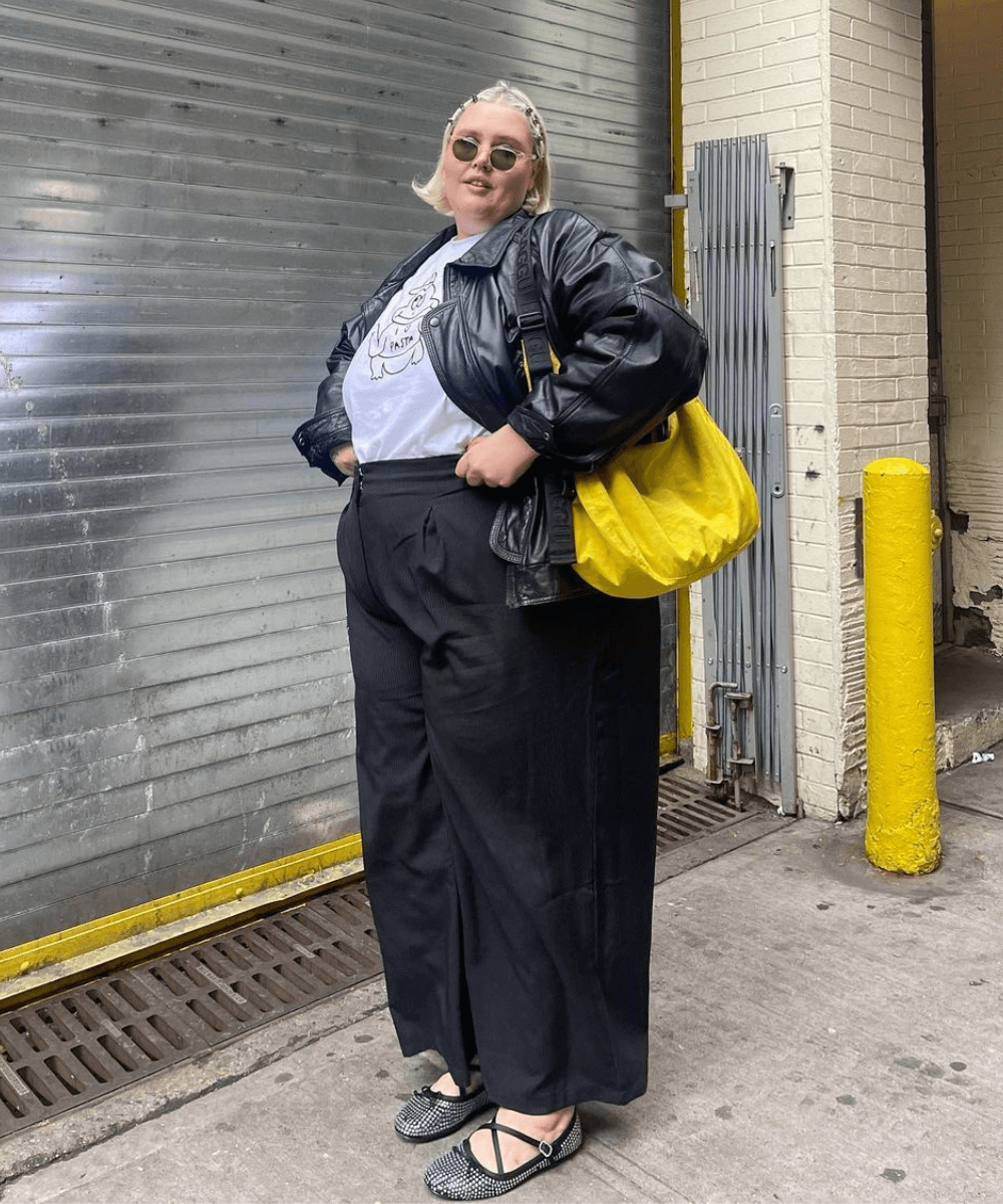 Abby Bible - calça preta alfaitaria, t-shirt estampada, jaqueta de couro e sapatilha brilhante - jaqueta de couro - inverno - mulher em pé na rua - https://stealthelook.com.br