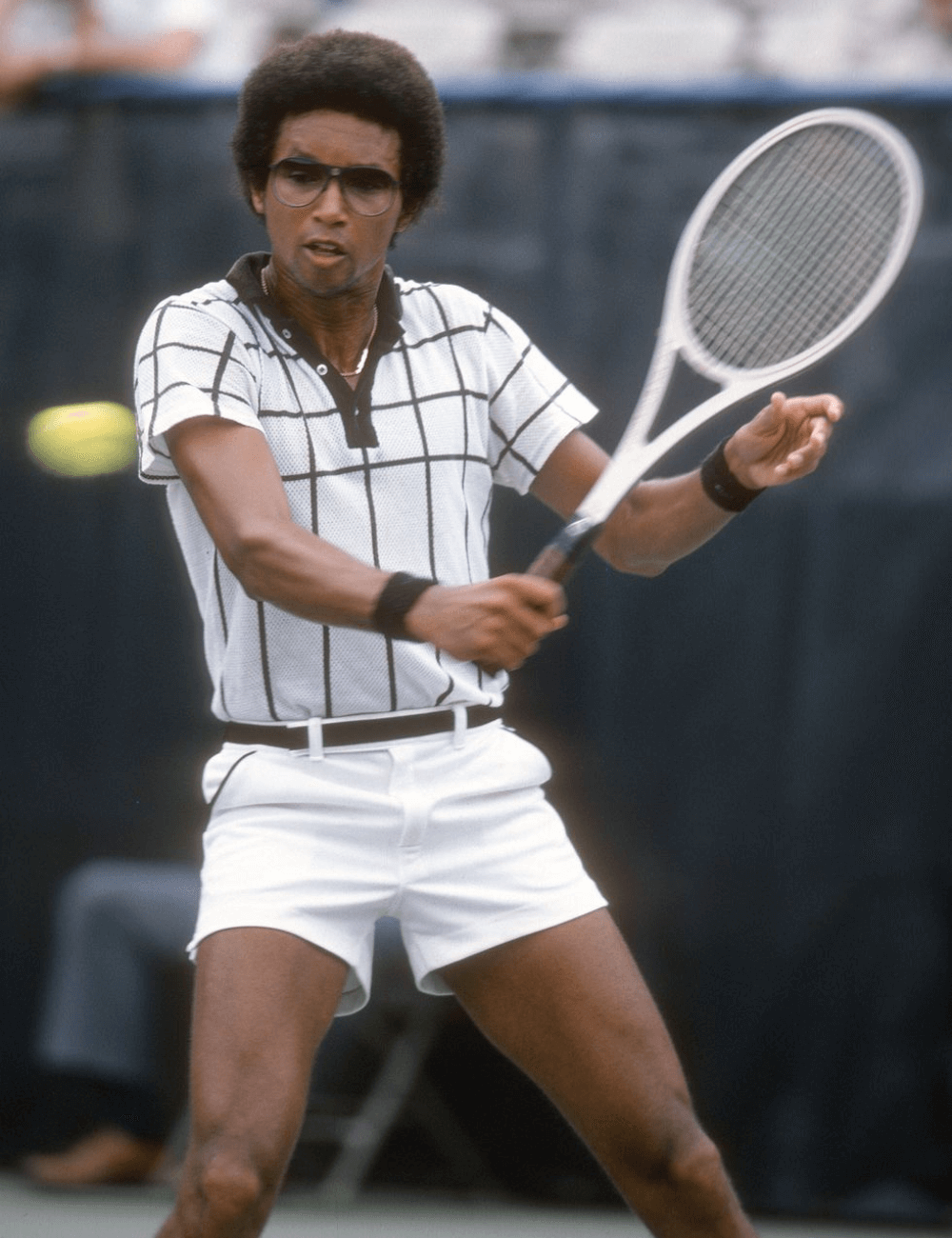 Arthur Ashe - shorts curto, blusa polo, munhequeiras e óculos - moda e tênis - verão - homem negro jogando tênis - https://stealthelook.com.br