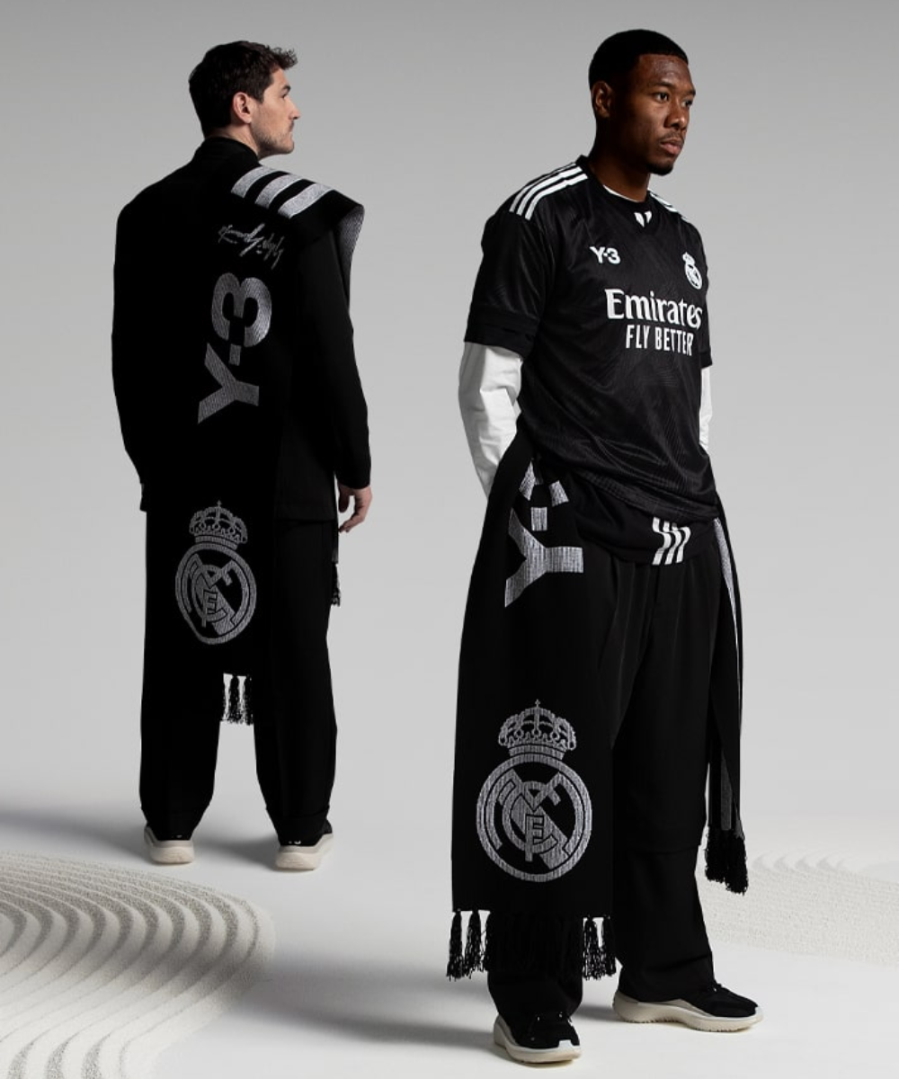 Real Madrid x Yohji Yamamoto - roupas diversas pretas - moda e futebol - verão - a foto mostra dois homems parados em pé usando uniformes pretos de futebol com o brasão da equipe, o 