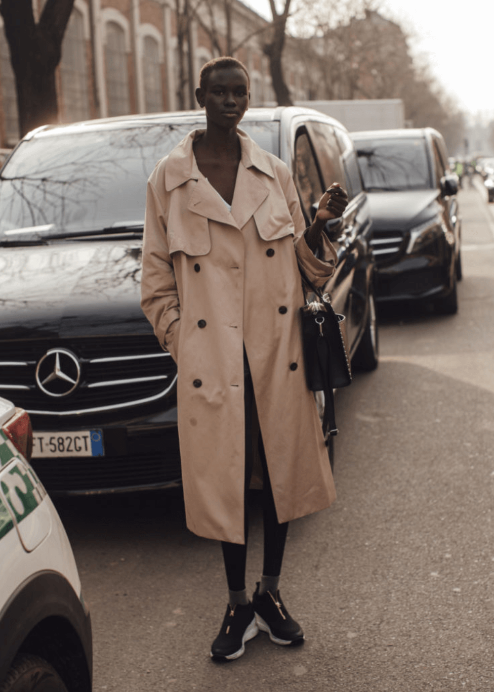 Street Style de Milão - trench coat bege, tênis e bolsa preta - street style de Milão - inverno - mulher negra em pé na rua - https://stealthelook.com.br