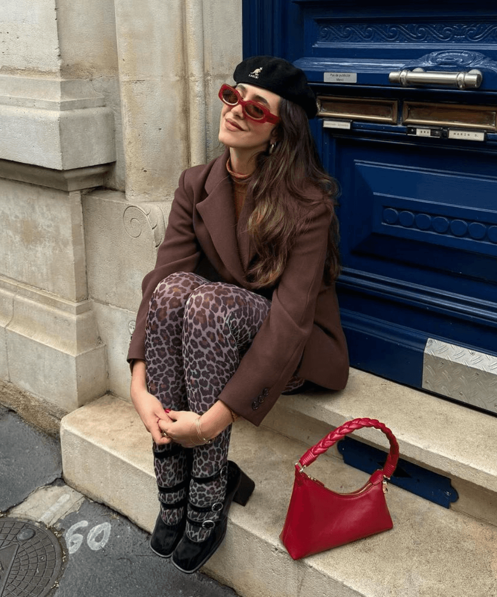 @florettenacer - meia-calça de onça, casaco marrom, boina, óculos e sapato boneca - tendências do inverno 2024 - inverno - mulher de óculos sentada na rua - https://stealthelook.com.br