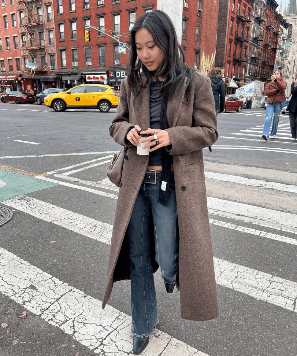 @vivian.yrl - calça jeans, regata preta, casaco marrom longo e lenço preto - tendências do inverno 2024 - inverno - mulher asiática andando na rua - https://stealthelook.com.br