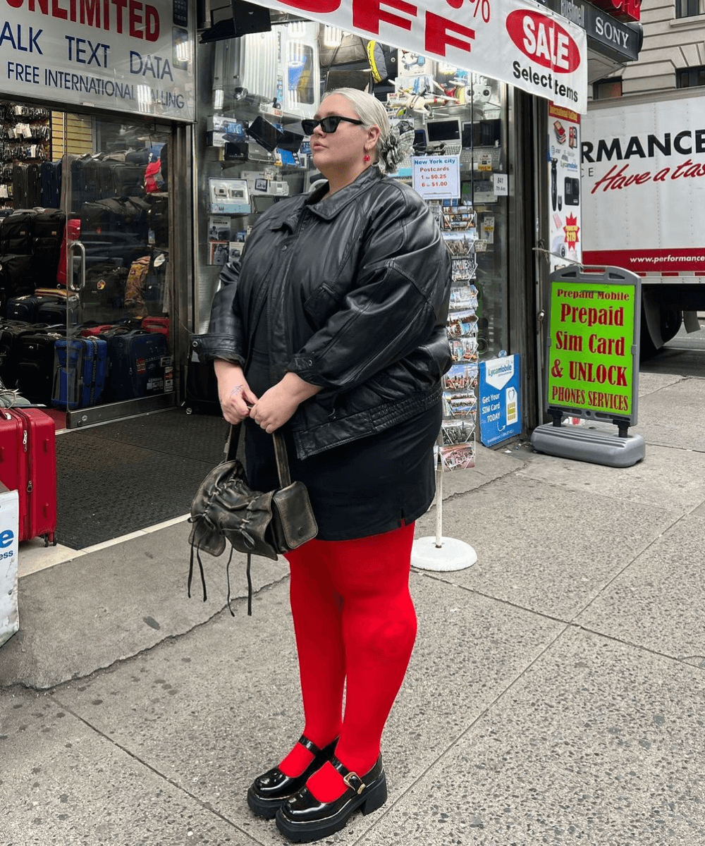 Abby Bible - meia-calça vermelha, sapato preto, minissaia preta, jaqueta e óculos - tendências do inverno 2024 - inverno - mulher loira em pé na rua de lado - https://stealthelook.com.br