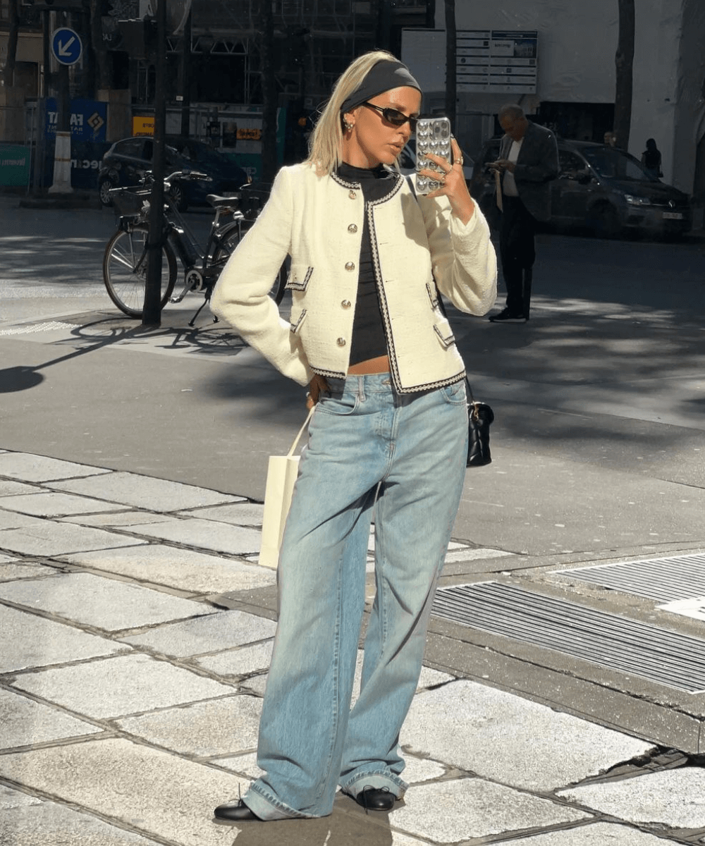Sofia Coelho - calça jeans, blusa preta, casaco off white e óculos preto - acessório tendência - inverno - mulher loira em pé na rua tirando foto em um espelho - https://stealthelook.com.br
