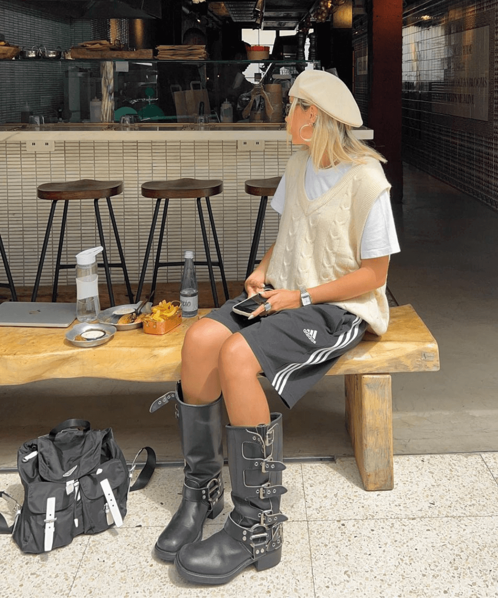 Sofia Coelho - bermuda preta, colete amarelo pastel, blusa branca e biker boots - biker boots - verão - mulher de boina sentada em um banco na rua - https://stealthelook.com.br