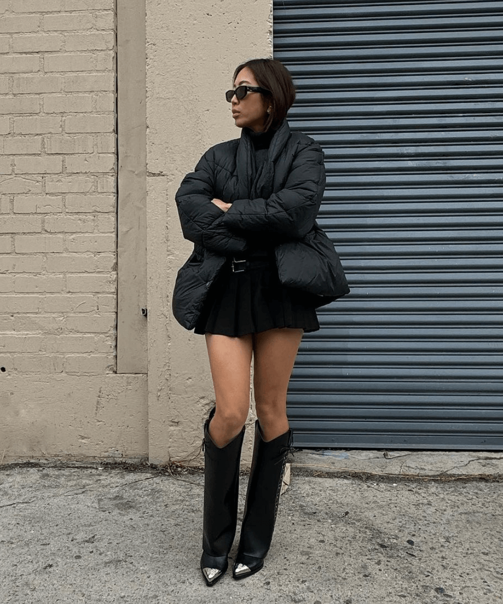 Aimee Song - minissaia plissada preta, bota de cano longo preta, jaqueta puffer preta - inverno 2024 - inverno - mulher asiática de pé na rua - https://stealthelook.com.br