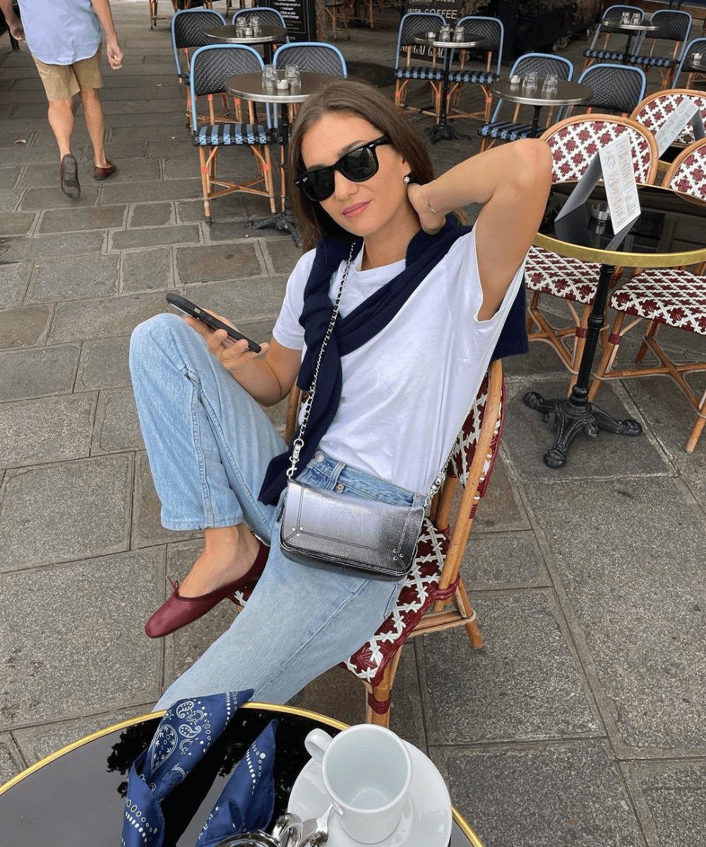 Adenorah | @annelauremais - calça jeans, camiseta branca, sapatilha vinho, óculos escuros e tricot amarrado no ombro - jeans e camiseta - outono - mulher de óculos sentada em um café na rua - https://stealthelook.com.br