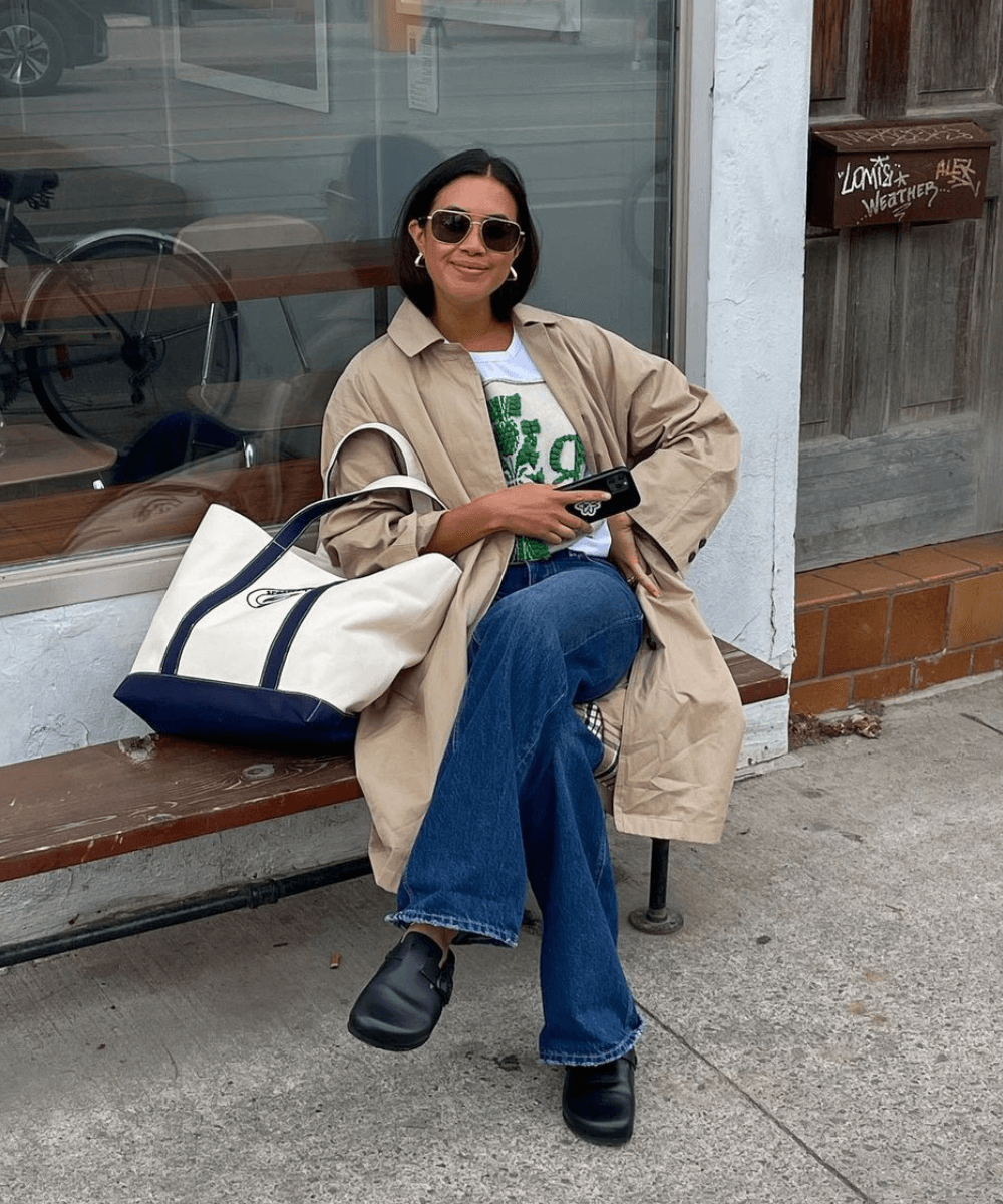 Sasha Mei - calça jeans, t-shirt estampada, trench coat e mule preto - jeans e camiseta - outono - mulher asiática de óculos sentada em um banco na rua - https://stealthelook.com.br