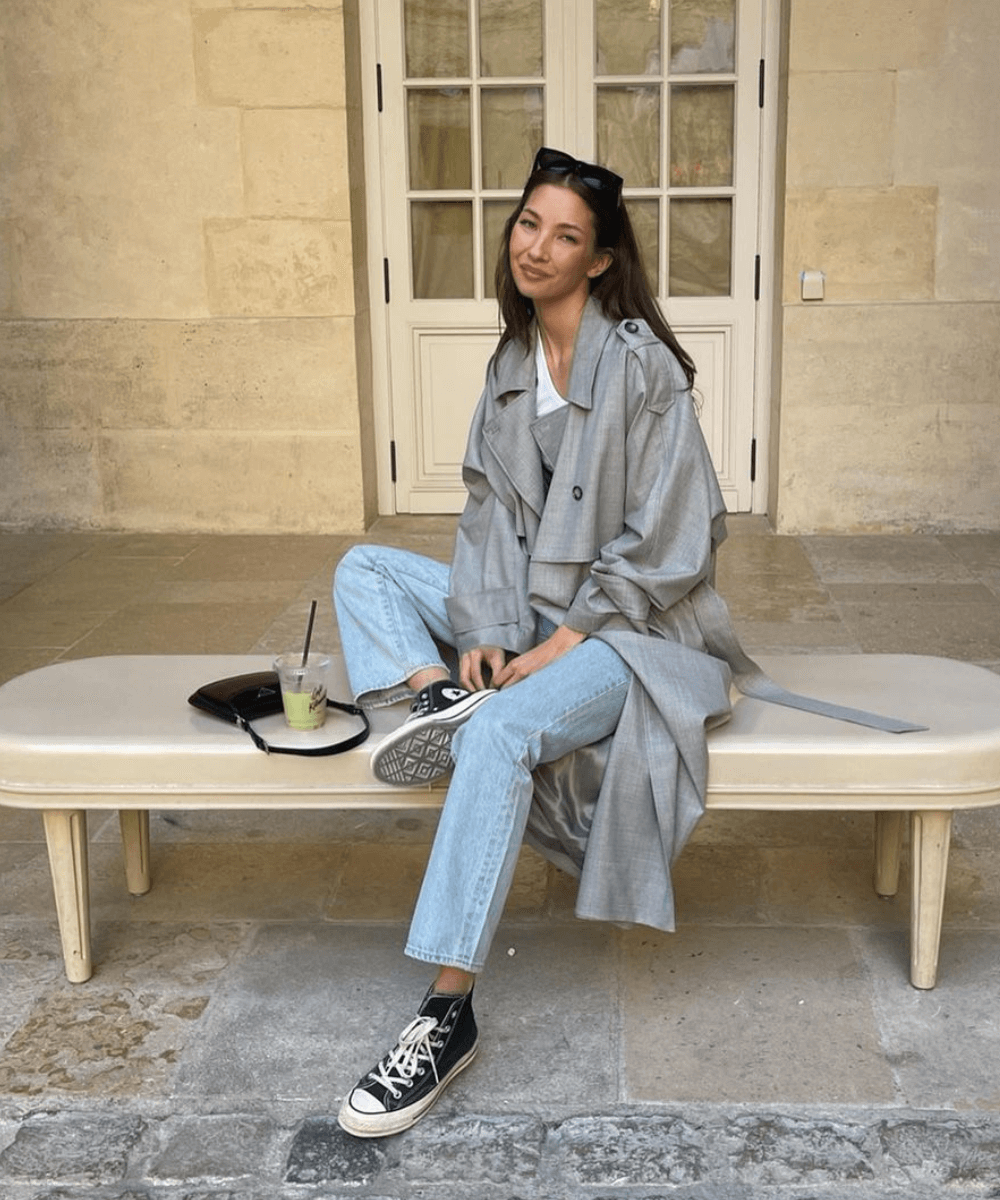 Felicia Akerstrom - calça jeans, converse e trench coat cinza - looks com tênis - outono - mulher sentada em um banco na rua - https://stealthelook.com.br