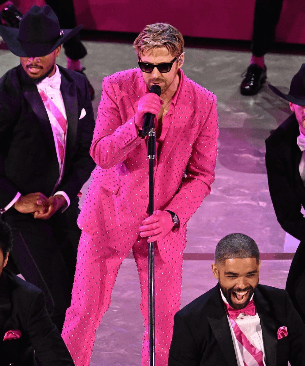 Ryan Gosling - terno rosa - melhores momentos do Oscar - inverno - homem loiro de óculos de sol cantando em um palco - https://stealthelook.com.br