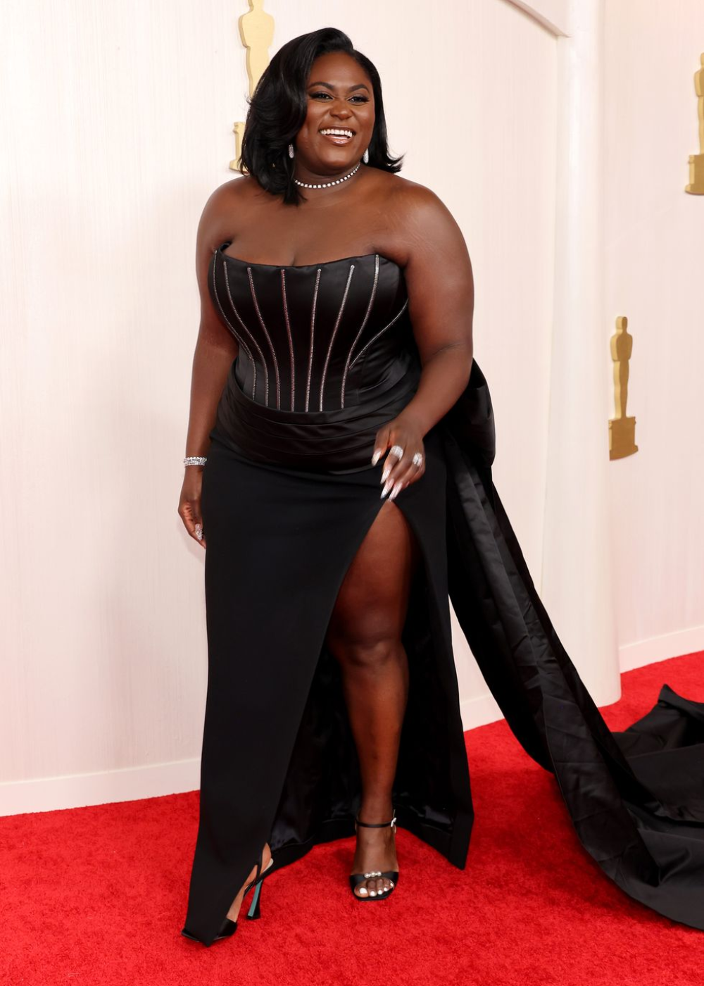 Danielle Brooks - vestido preto sem alças e fenda nas pernas - Oscar 2024 - inverno - mulher negra em pé sorrindo no tapete vermelho - https://stealthelook.com.br